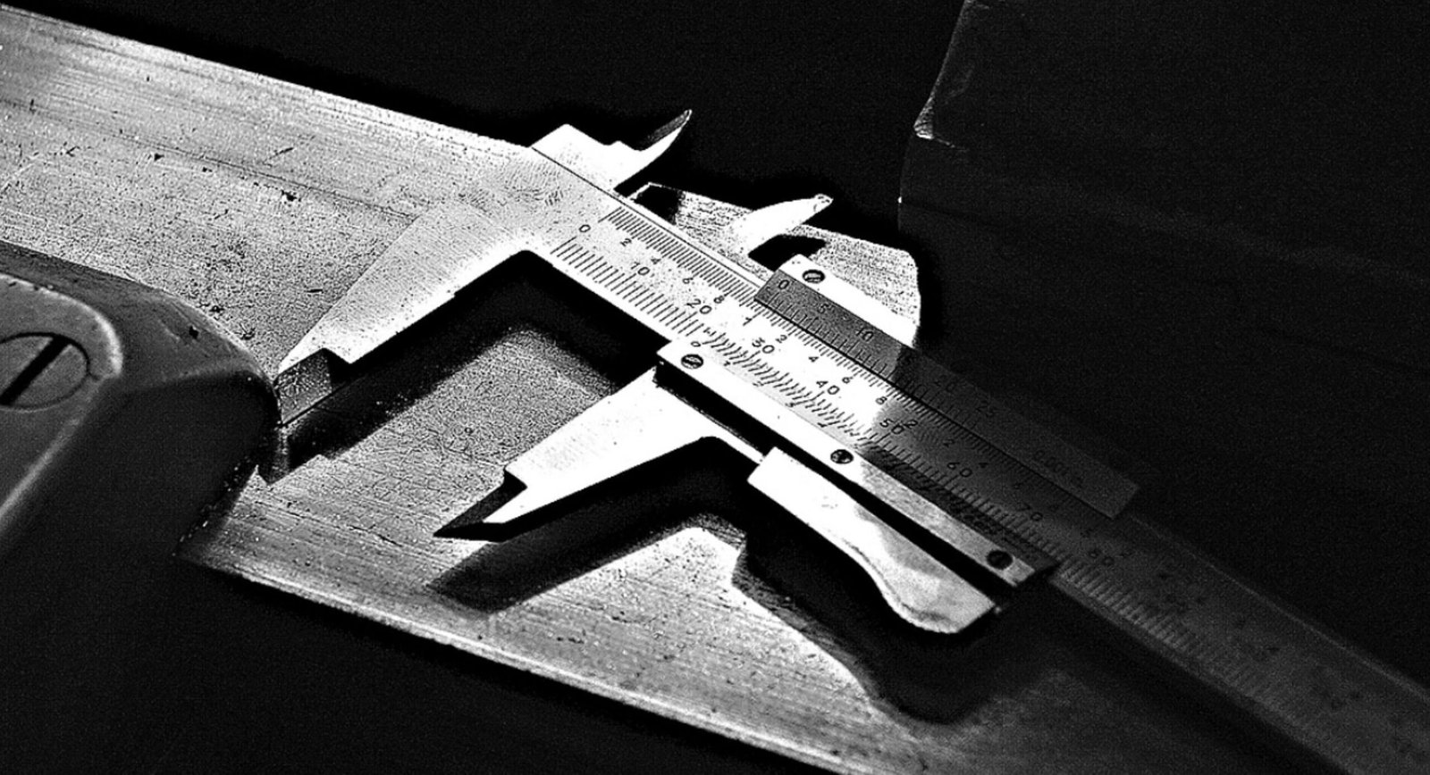 Precision calipers measuring a metal surface in a low-light setting